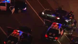 Multiple police officers contacting persons on the street, with a police vehicle’s emergency lights    